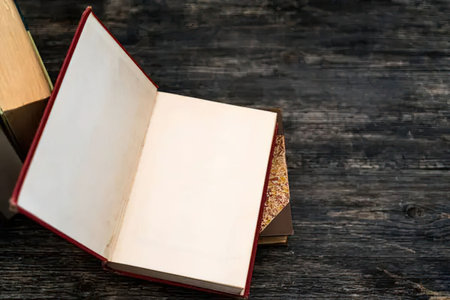Open red leather bound book with blank white pages lies on a wooden table surrounded by other books.