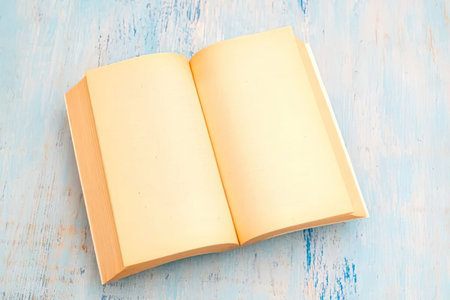 Open blank book with yellow pages lies on a distressed blue wooden surface, symbolizing a rustic and...
