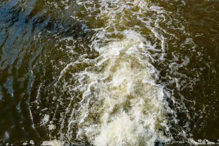 Foamy white waves and ripples flow over the turbulent greenish brown water creating a dynamic...