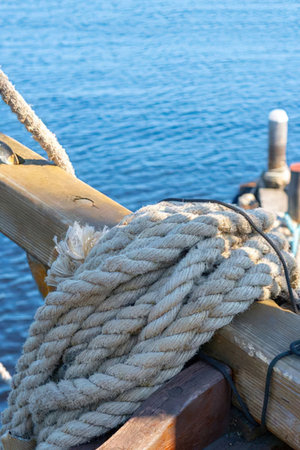 Thick rope is tied around a wooden dock post with a secure knot on a calm sunny day.