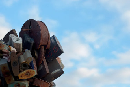 Rusted industrial machinery parts form a unique sculpture against a serene cloudy blue sky, creating...