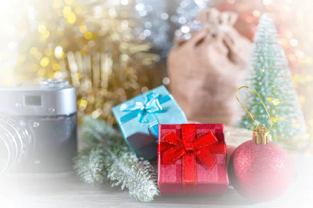 Christmas gifts and decorations are arranged on a table with a camera in the soft background.