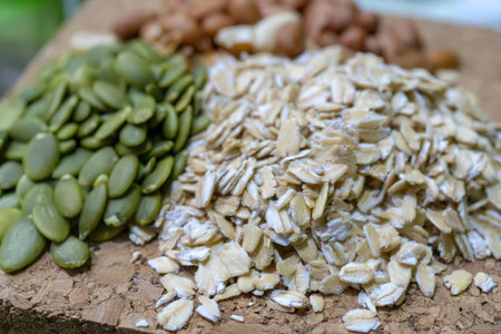 Assortment of healthy dry cereals and seeds like pumpkin seeds and oatmeal are arranged on a wooden...