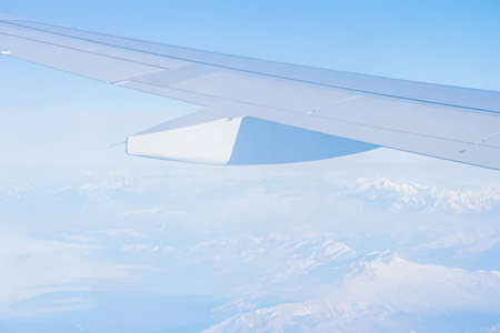 Airplane wing soaring above white clouds against a clear blue sky as it flies at high altitude.