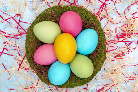 Colorful easter eggs are arranged in a nest surrounded by red and white shredded paper decorations.