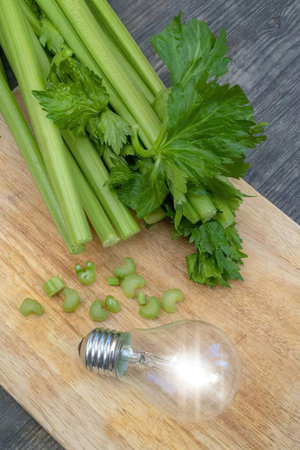 Fresh celery stalks with leaves on a wooden cutting board surrounded by chopped celery and a...