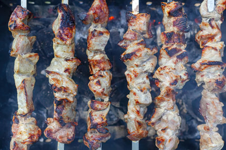 Grilled pork skewers sizzle on barbecue grill, featuring charred and juicy meat pieces, perfectly...