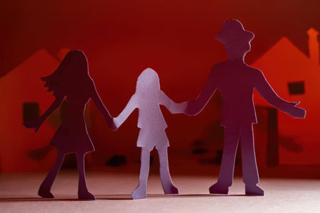 Happy family of three paper cutout figures holding hands together in front of a house with a bright...
