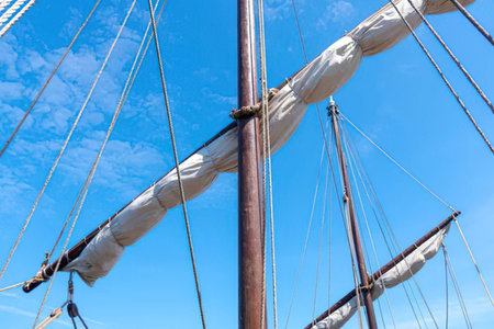 Majestic sailing ship mast stands tall with furled white sails against a clear blue sky, evoking a...
