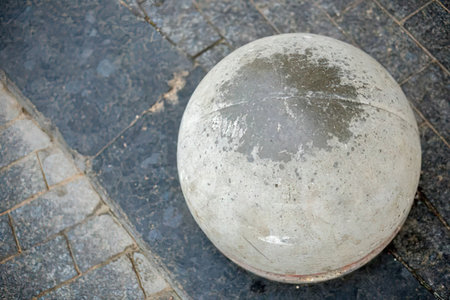 A large worn stone sphere sits on a dark cobblestone street showing signs of aging and weathering...