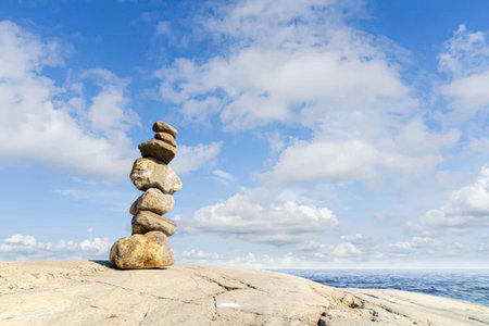 Stack of balanced rocks on a rocky surface against a serene blue cloudy sky evoking a sense of...