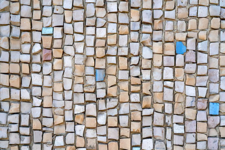 Mosaic pattern made with small beige marble tiles and some blue pieces filling gaps on wall creating...