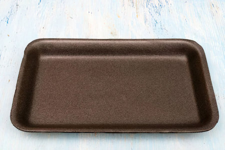 Brown rectangular baking tray is placed on a light blue wooden surface with visible wood grain and...