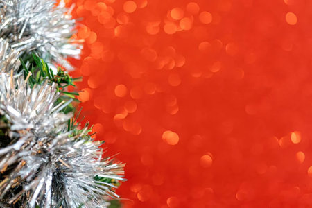 Christmas tree branch adorned with shiny silver tinsel set against a vibrant red background with...