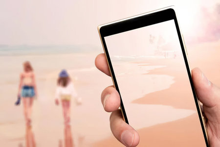 Person captures serene beach scene on smartphone screen while walking along the sandy shore with...
