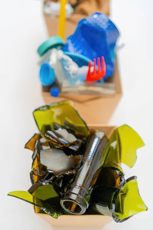 Broken green glass and plastic items are sorted into cardboard boxes for recycling and...