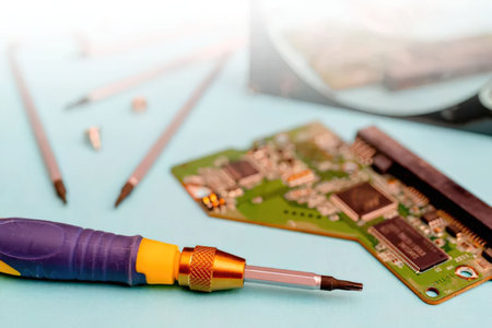 Screwdriver is positioned on a blue work surface alongside an electronic circuit board and various...