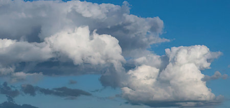 Large white fluffy cumulus clouds drift lazily across a clear blue sky accompanied by scattered...