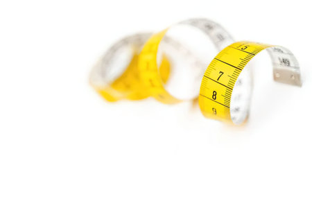 Yellow and white measuring tape curled and isolated on a white background representing health and...
