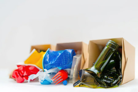 Plastic waste and empty bottles are carelessly disposed of in cardboard boxes on a white background,...