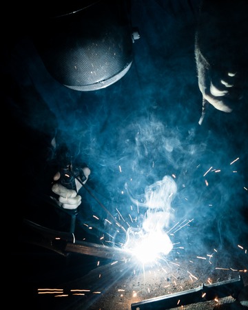 Man welding iron with a protective mask. Dramatic sparkles and smokeの写真素材