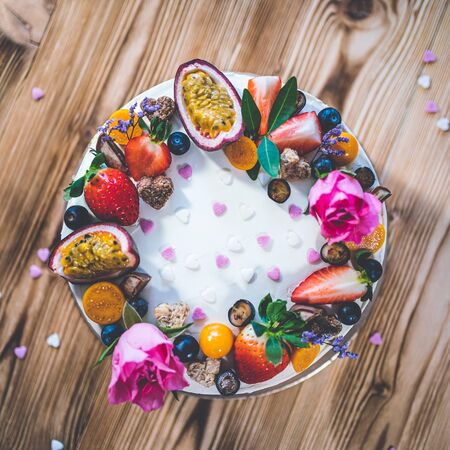 Sweet white cheesecake torte with fresh fruits, poppy and rose flowers on wooden table background. Ideal gift for birthday, Valentine day and celebrationの写真素材