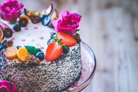 Sweet white cheesecake torte with fresh fruits, poppy and rose flowers on wooden table background. Ideal gift for birthday, Valentine day and celebrationの写真素材