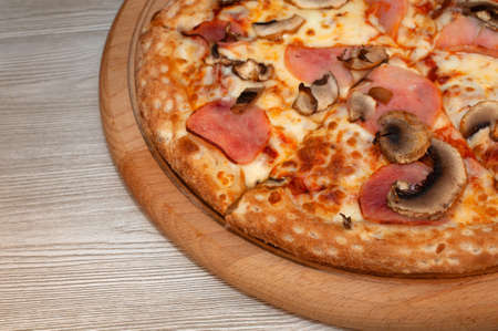 Pizza with ham, mushrooms and cheese on a boardの写真素材
