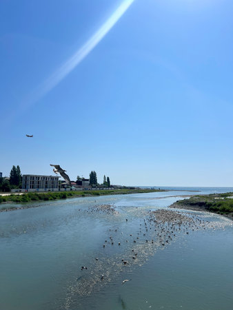 Plane flies over the river and housesの写真素材