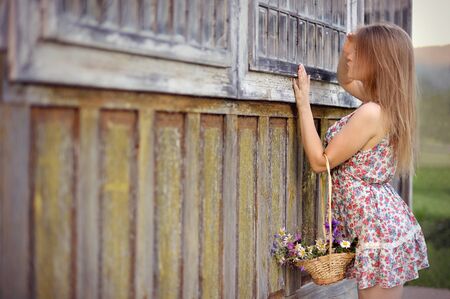 Romantic girl with a basket look window on the rustic porchの写真素材
