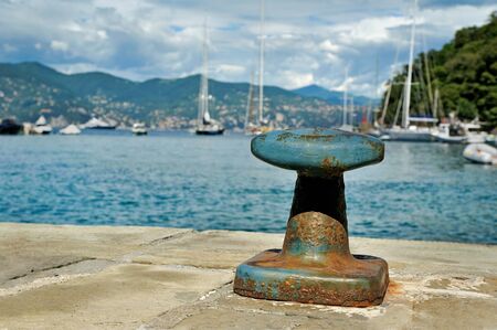 Mooring post in Portofino harbor with yachts cloudly sky backgroundの写真素材