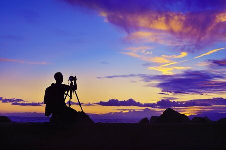 silhouette of photographer taking photo at violet sunset beside the seaの写真素材