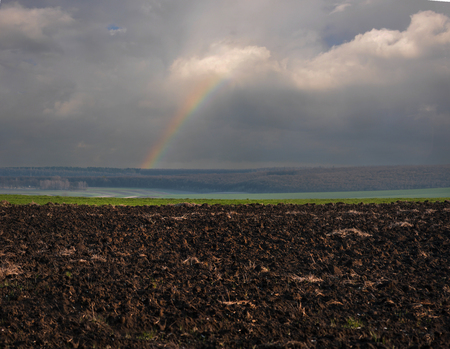 brown arable soil land in the field at early spring time with rainbow at the skyの写真素材