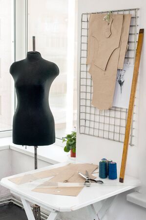 workplace with sewing equipment, fabrics, patterns, sewing studio with dummy and clothes hangers,...