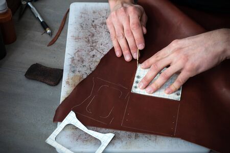 High angle view of caucasian male hand master cutting with a knife pattern from genuine leather....