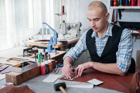 Man working with leather at a workshop. Handmade craft production cutting with patterns