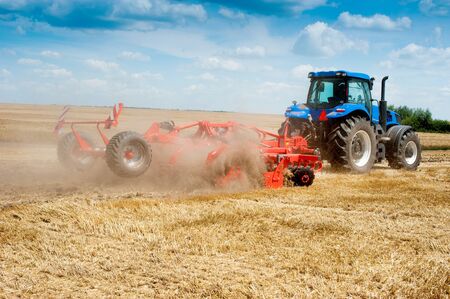 blue tractor working in the field, agricultural machinery work, tractor with harrow against a cloudy...