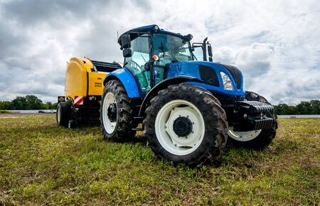 new blue tractor with Baler Roll belt in motion at demonstration field site at agro exhibition.