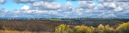 Spring panoramic view of plowed land and village at horizon with cloudy sky