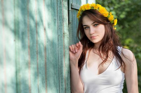 young girl in a wreath of dandelions in the spring garden, wooden rural backgroundの写真素材