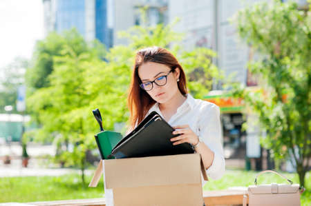 girl with glasses looking for a new job through dismissal, a box with foldersの写真素材