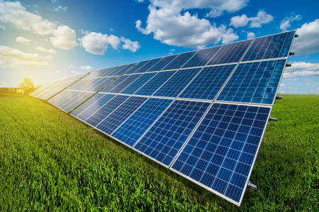 Solar energy panel system power at green grass and sky with clouds and sunshine