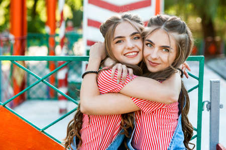 Beautiful teenage twin sisters in colorful clothes with lollipops huggingの写真素材