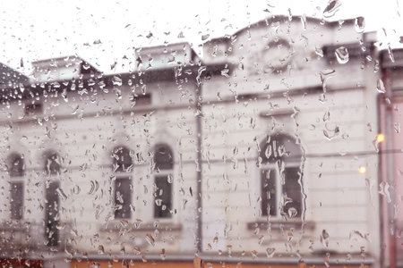 Rainy blurred window abstract, house visible through transparent wet rain drops on glass window out...