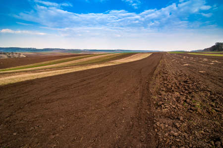 arable spring field, plowed soil and relief hilly, landscape in the backgroundの写真素材