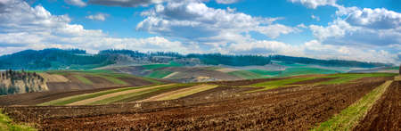 spring wide panorama of arable fields stretching to horizon under clear bright blue sky with clouds on distant hills. Agriculture and farming concept.の写真素材