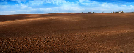 hills of plowed fields, soil prepared for sowing, farmhouse further on the horizonの写真素材