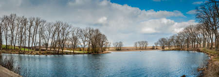 Wonderful landscape, early spring on a small lake, panorama. Reflection of reeds, sky and trees in the waterの写真素材