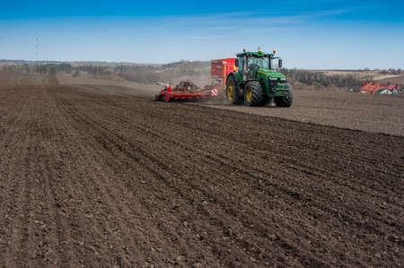 BAYKIVTSI, TERNOPIL REGION, UKRAINE - APRIL 10, 2021: Farmers sow, apply fertilizer using a John Deere 8370R tractor with a POTTINGER TERRASEM c8 seeder in a plowed fieldのeditorial素材