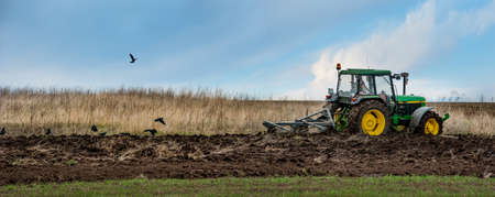 BAYKIVTSI, TERNOPIL REGION, UKRAINE - APRIL 20, 2021: a tractor 90s John Deere 2850 with a homemade plow prepares the field for sowingのeditorial素材